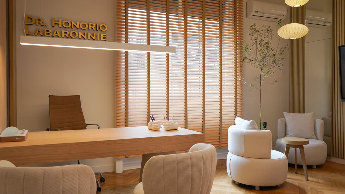 Sala de espera con sillones beige, mesa redonda de madera y mostrador de recepción al fondo